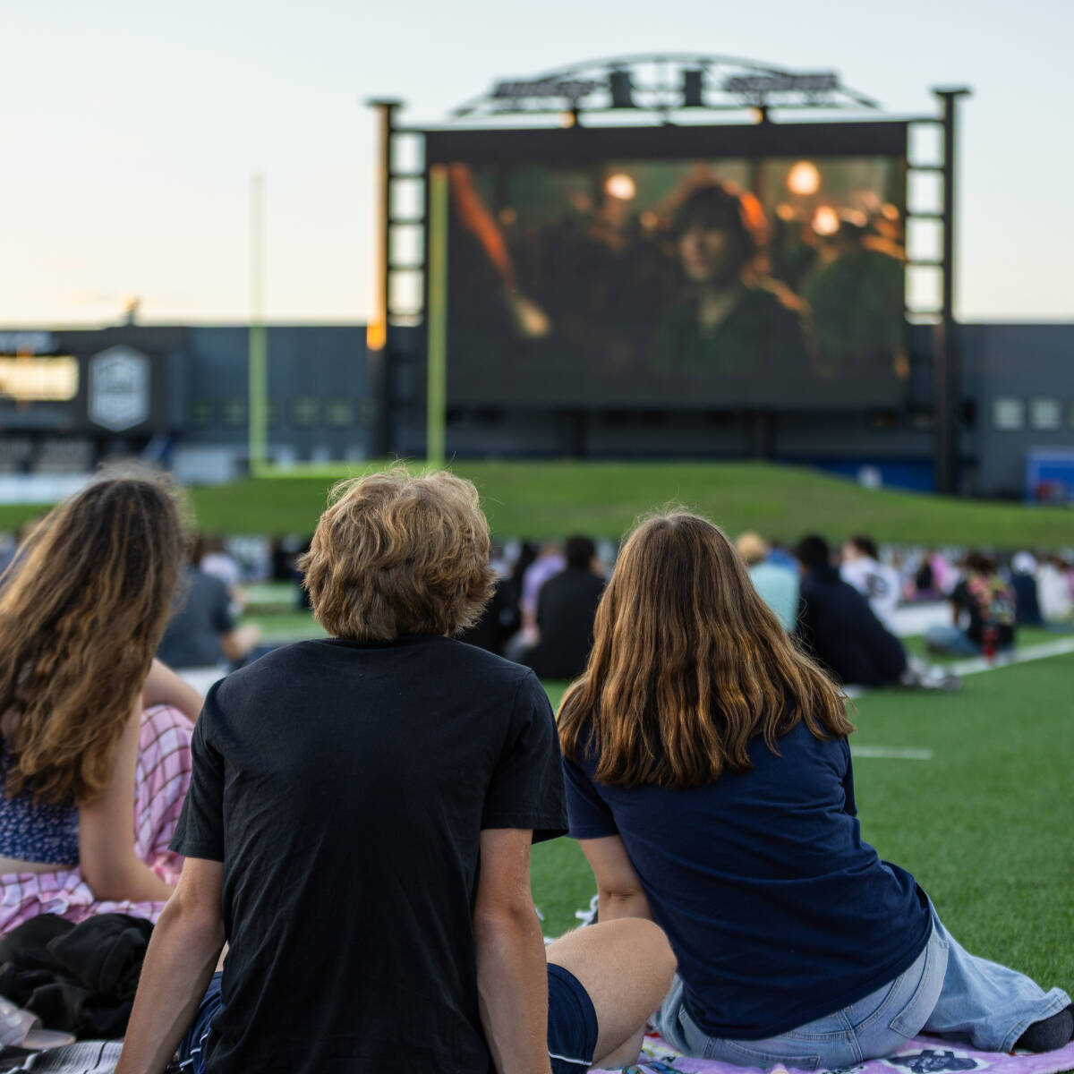 Students sitting on the field at Lubbers Stadium and watching a movie on the big screen